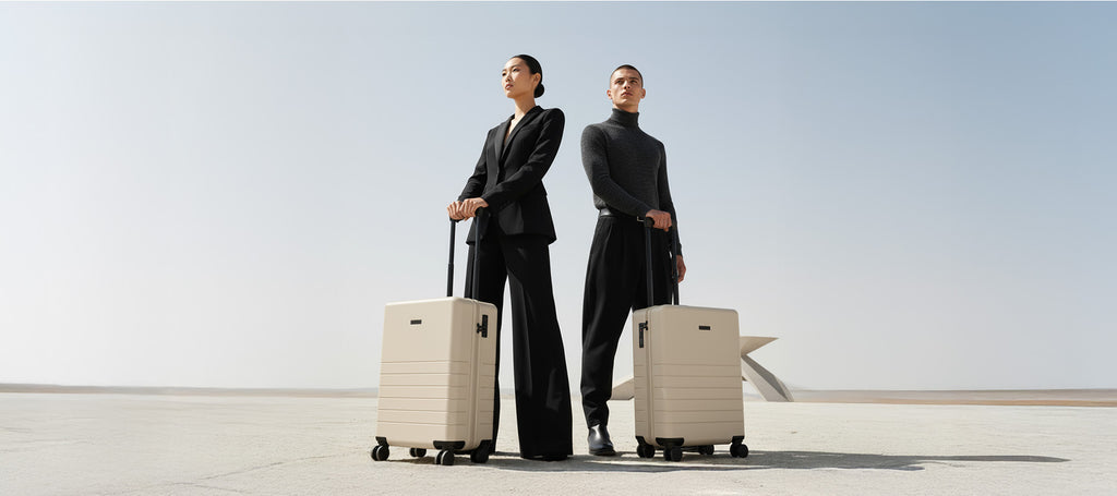 Handgepäckkoffer in creme mit zwei modernen Personen in schwarz gekleidet in der Wüste